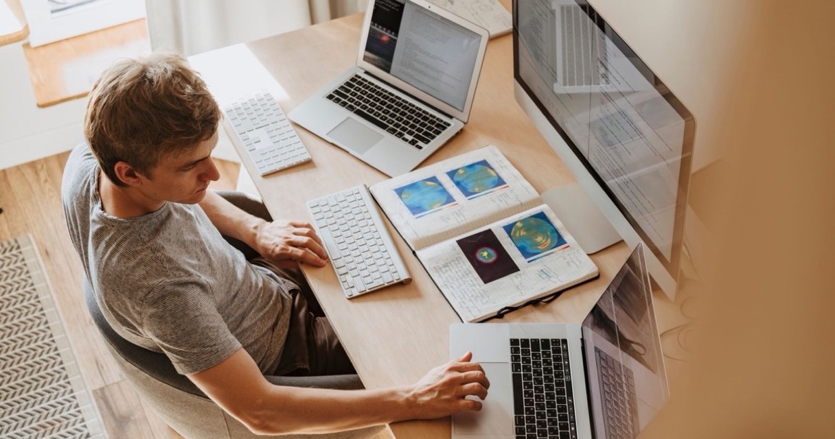 Desenvolvedor trabalhando em casa com dois notebooks e um monitor